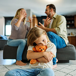 A sad girl hugs a teddy bear as parents argue, showing family conflict - Leonard Law Firm