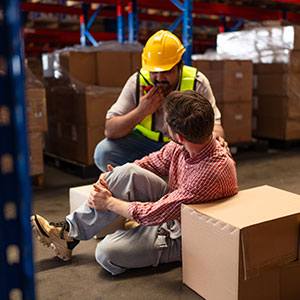 A worker helps an injured coworker in a warehouse, representing a workplace injury claim.